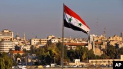 FILE - A Syrian national flag waves as vehicles move slowly on a bridge during rush hour, in Damascus, Syria, Feb. 28, 2016. 