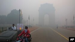  FILE - A man covers his face as he rides in front of the landmark India Gate, enveloped by smoke and smog, in New Delhi, India, Oct. 31, 2016.