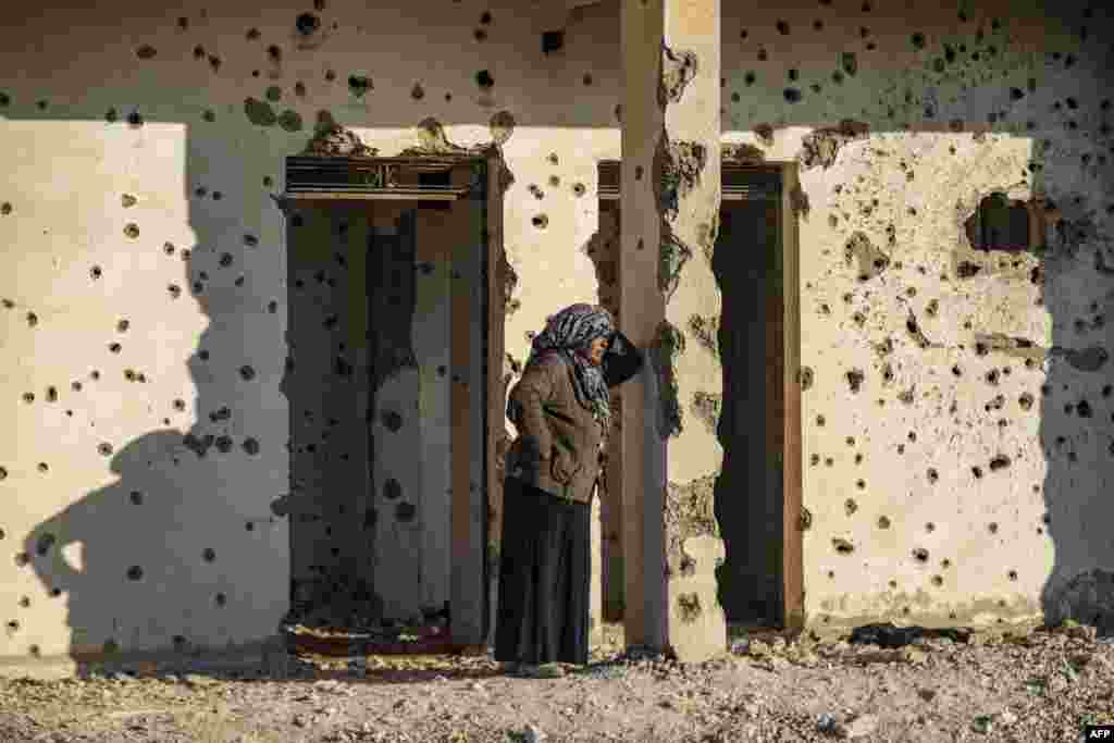 A Syrian Kurdish woman, fleeing from north of Aleppo, stands leaning on a bullet-riddled wall upon arriving in Tabqa, on the western outskirts of Raqa.