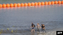 资料照片：移民们在德克萨斯州边境格兰德河边沿着一串橙色浮标行走。（2023年7月17日）