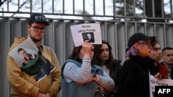 Prosvjednica drži plakat s natpisom "Putin ubija Rusiju" i prikazuje sliku Alekseja Navaljnog tijekom odavanja počasti njemu ispred ruskog veleposlanstva u Beogradu, 16. februara 2024.