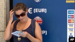 FILE - A woman stands by a currency exchange ATM in Madrid, Spain, June 9, 2017. 