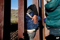 FILE - A Honduran migrant helps a youth squeeze through the U.S. border wall over to San Diego, California, from Playas in Tijuana, Mexico.