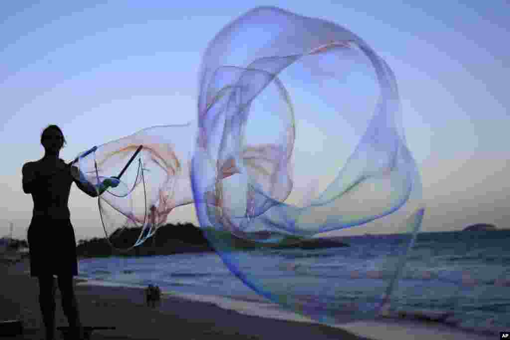 Seniman jalanan Florian Timm membuat gelembung sabun raksasa di pantai Ipanema, Rio de Janeiro, Brazil.