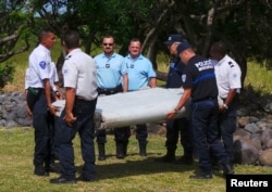 French gendarmes and police carry a large piece of plane debris which was found on the beach in Saint-Andre, on the French Indian Ocean island of La Reunion, July 29, 2015.