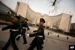 FILE - Chinese paramilitary police march past China's central bank, the People's Bank of China, in Beijing, March 12, 2016.