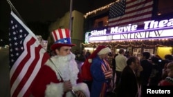 Matt Ornstein, mengenakan kostum Sinterklas, memegang bendera Amerika saat para pengunjung antri membeli tiket untuk menonton pemutaran perdana film "The Interview" di Los Angeles, California (24/12).