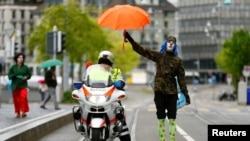 A person dressed as a clown holds an umbrella over a police officer in Switzerland, 2017.