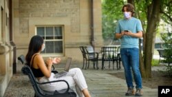 In this photo, Bryan Maley, right, a grad student, interviews a student on campus about mask-wearing experiences as part of a public health survey, Friday, July 30, 2020, in Ithaca, N.Y. (Jason Koski/Cornell University via AP)