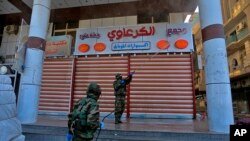 Workers in protective suits spray disinfectant as a precaution against the coronavirus, in a commercial district in Najaf, Iraq, Feb. 26, 2020. 