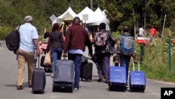 A family from Haiti approaches a tent in Saint-Bernard-de-Lacolle, Quebec, stationed by Royal Canadian Mounted Police, as they haul their luggage down Roxham Road in Champlain, N.Y., Aug. 7, 2017.