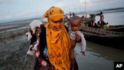 FILE - A Rohingya woman carries a child after crossing a stream on a small boat near Cox's Bazar's Dakhinpara area, Bangladesh, Sept. 21, 2017.