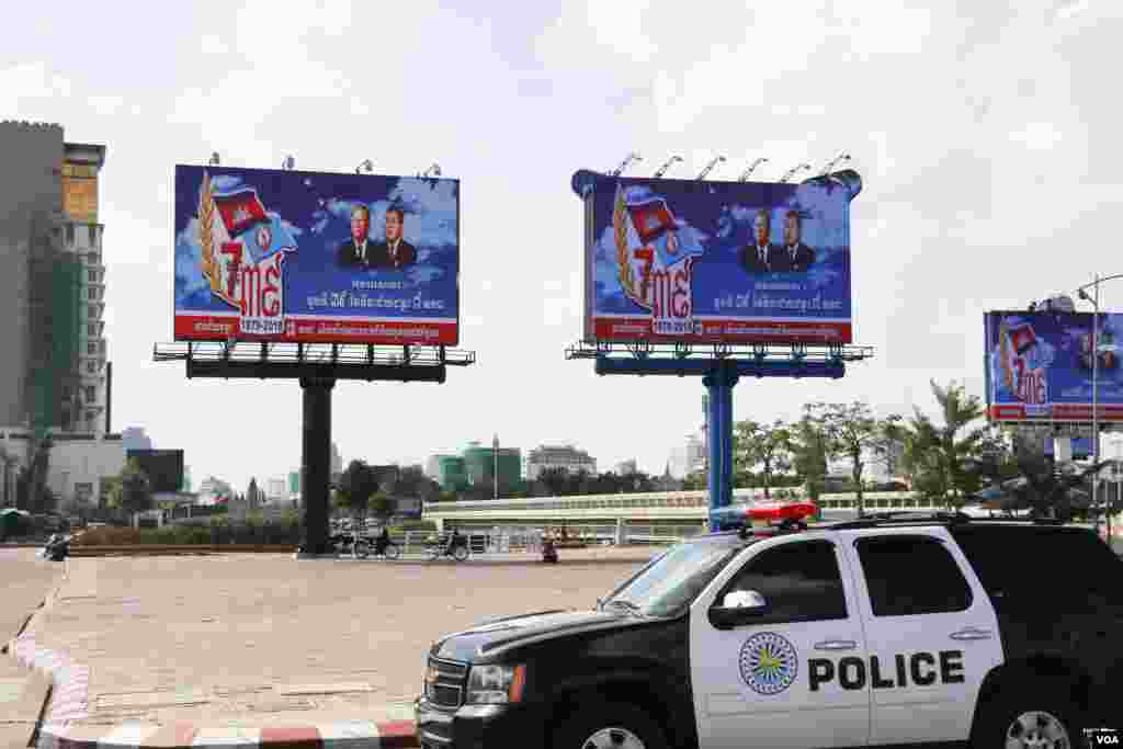 រថយន្ត​នគរបាល​ជិះ​តាម​ផ្លូវ​នៅ​កោះពេជ្រ កាត់​ផ្ទាំងអបអរ​សាទរ​ទិវា ៧មករា ដែល​មាន​រូប​លោក​នាយករដ្ឋមន្រ្តី ហ៊ុន សែន និង​ប្រធាន​រដ្ឋសភា លោក ហេង សំរិន នៅ​រាជធានី​ភ្នំពេញ កាលពីថ្ងៃទី៦ ខែមករា ឆ្នាំ២០១៨។ (ស៊ុន ណារិន/VOA)