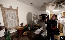 FILE - A journalist videotapes a wall tapestry displaying religious writing in the living room of an apartment in Redlands, Calif., shared by San Bernardino shootings suspects Syed Farook and his wife, Tashfeen Malik, Dec. 4, 2015.