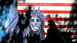 FILE - An Iranian woman walks past graffiti art characterizing the U.S. Statue of Liberty, painted on the wall of the former U.S. Embassy in Tehran, Iran, Sept. 25, 2007. An Iranian-American businessman and his father, who are serving 10-year prison sentences in Iran over their ties to the U.S., have lost a court appeal, a lawyer said Monday, Aug. 28, 2017. 