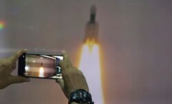 A man at New Delhi's Nehru Planetarium, takes pictures of a web cast of the lift off of Indian Space Research Organization (ISRO)'s Geosynchronous Satellite launch Vehicle (GSLV) MkIII carrying Chandrayaan-2 from the Satish Dhawan Space Center.