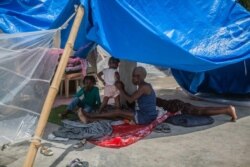 A woman and kids rest in the shade at a camp for people who lost their home during the Aug. 14 earthquake in Les Cayes, Haiti, Aug. 23, 2021.
