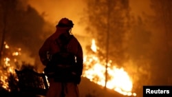 A firefighter watches flames advance up a hill toward homes as crews battle the Carr Fire, west of Redding, Calif., July 27, 2018.