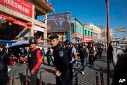 In this Nov. 3, 2017 file photo, armed civilians patrol the area outside the Hotan Bazaar where a screen shows Chinese President Xi Jinping in Hotan in western China's Xinjiang region.