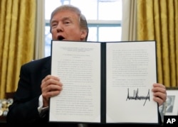 President Donald Trump holds up one of the Section 201 actions that he signed during a ceremony in the Oval Office of the White House in Washington, Tuesday, Jan. 23, 2018. Trump says he is imposing new tariffs to "protect American jobs