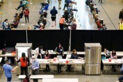 FILE - People work near refrigerators used to store the Pfizer vaccine for COVID-19, as patients who have received the shot sit in an observation area during a one-day vaccination clinic set up in an Amazon.com facility in Seattle, Jan. 24, 2021.