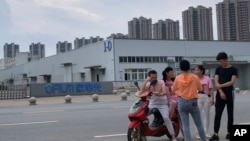 In this June 5, 2019, photo, neighborhood residents chat near the entrance to an OFILM factory in Nanchang in eastern China's Jiangxi province. (AP Photo/Ng Han Guan)