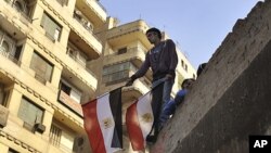 A young Egyptian man holds a national flag while standing on a rooftop between Tahrir Square and the Interior Ministry in Cairo, Egypt, Nov. 26, 2011.