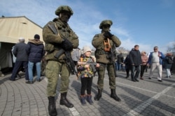 FILE - A child poses for a picture with Russian servicemen during a military equipment and hardware show, on Defender of the Fatherland Day, in Sevastopol, Crimea, Feb. 23, 2020.