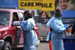Wearing a gown, mask and gloves, critical care nurse Molly Spaeny, left, with St. Vincent Healthcare speaks with a patient after administering a coronavirus test in a drive-thru testing center outside the hospital in Billings, Mont., March 20, 2020.