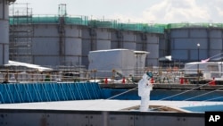 FILE - A worker, wearing a protective suit and mask, takes notes in front of storage tanks for radioactive water at the tsunami-crippled Fukushima Dai-ichi nuclear power plant, operated by Tokyo Electric Power Co. (TEPCO), in Okuma, Fukushima Prefecture, Japan.