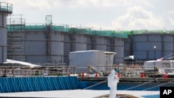 FILE - A worker, wearing protective gear, takes notes in front of storage tanks for radioactive water at the tsunami-crippled Fukushima Daiichi nuclear power plant in Okuma, Japan, Feb. 10, 2016. 