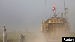 FILE - A man gestures at U.S military vehicles driving in the town of Darbasiya next to the Turkish border, Syria, April 28, 2017. 