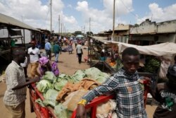 FILE - Vendors look at cabbage loaded on the back of a tricycle, as it is brought to the market to be sold in the town of Kiu, south of Nairobi, Kenya, Jan. 12, 2020.