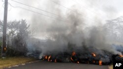 Lava crosses the road near Pohoiki Road, May 18, 2018, near Pahoa, Hawaii. Several open fissure vents are still producing lava splatter and flow in evacuated areas. Gas is also pouring from the vents, cloaking homes and trees in smoke. 