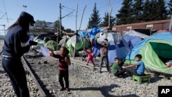 Grčki policajac daje papir s informacijama detetu u improvizovanom kampu na severu zemlje, u blizini Idomenija 