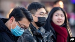 Travelers wear face masks as they walk outside of the Beijing Railway Station in Beijing, Jan. 20, 2020.