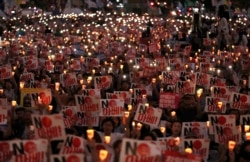 Protesters hold candles and signs during a rally denouncing Japanese Prime Minister Shinzo Abe and also demanding the South Korean government cancel its GSOMIA agreement with Japan, in downtown Seoul, South Korea, Aug. 15, 2019.