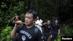 Members of a police forensic team carry a body bag with human remains dug from the grave near the abandoned human trafficking camp in the jungle close the Thailand border at Bukit Wang Burma in northern Malaysia May 27, 2015.