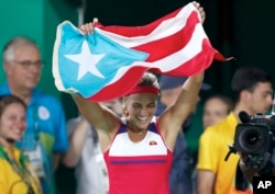 Monica Puig of Puerto Rico celebrates holding her country's flag after winning the gold medal match in the women's tennis competition at the 2016 Summer Olympics in Rio de Janeiro, Brazil, Saturday, Aug. 13, 2016.
