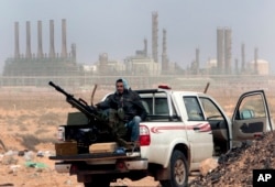 FILE - An anti-government rebel sits with an anti-aircraft weapon in front an oil refinery in Ras Lanouf, eastern Libya, March 5, 2011.