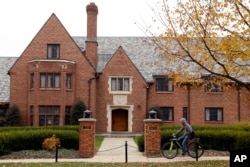 FILE – In this Nov. 9, 2017, photo, a bicyclist rides past Penn State's shuttered Beta Theta Pi fraternity house in State College, Pa. The parents of Penn State student Tim Piazza, 19, who died in a hazing ritual while pledging for Beta Theta Pi, reached a settlement in September 2018 with the fraternity's national organization that provides for reforms. The Beta Theta Pi chapter was permanently banned by the university.