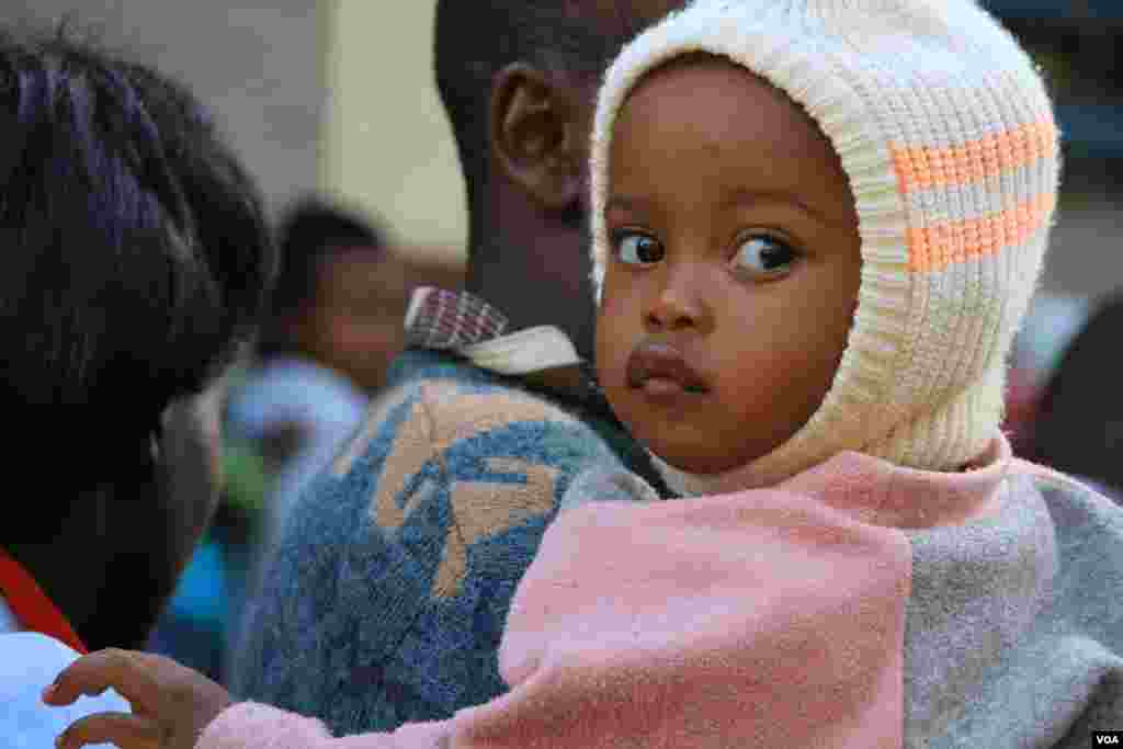 A father carries his daughter as he waits his turn to vote at the Mutomo Primary School, March 4, 2013. (J. Craig/VOA) 