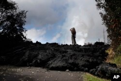 Hannique Ruder, 65, a resident of the Leilani Estates subdivision, stands on a mound of hardened lava near Pahoa, Hawaii, May 11, 2018. The Kilauea volcano has destroyed more than 35 structures since it began releasing lava from vents about 25 miles (40 kilometers) east of the summit crater.