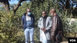 Journalists Samuel Takawira and Frank Chikowore stand with a police detective outside a court in Harare, Zimbabwe, May 23, 2020. (Columbus Mavhunga/VOA) 