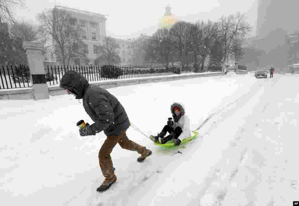 John Joy menarik pacarnya Brooke Finan melewati gedung pemerintahan setelah mencari kopi dalam badai salju di Boston, Massachusetts (27/1). ​(AP/Steven Senne)