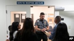 Полицаец слуша прашање додека ги насочува луѓето во судница во судот за имиграција во Мајами, Флорида, 10 јануари 2024 година.