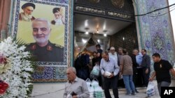 FILE - People leave a mosque in a predominantly Iraqi neighborhood, south of Tehran, Iran, July 30, 2019. A poster of Gen. Qassem Soleimani is on the wall, with the Ayatollah Khomeini, top left, and Supreme Leader Ayatollah Ali Khamenei.