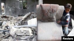 Seorang anak laki-laki memegang kursi di antara reruntuhan gedung yang hancur akibat serangan udara di kota yang dikuasai pemberontak, Mesraba, di Ghouta timur Damaskus, Suriah, 26 November 2017. 