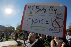 A woman carries a sign opposing mandates for the vaccine against the COVID-19 at a "Rise Against Tyranny" event in Boston, Massachusetts, Nov. 7, 2021.