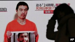 A passerby is silhouetted against a large TV broadcasting a news program showing a still photo of Japanese hostage Kenji Goto holding what appears to be a photo of Jordanian pilot Mu'ath al-Kaseasbeh, in Tokyo, Jan. 28, 2015.